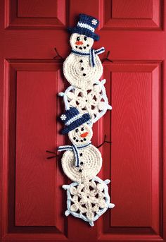 a crocheted snowman hanging on a red door with two hats and scarfs