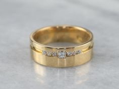 two gold wedding bands with diamond stones on the top and bottom, sitting on a marble surface