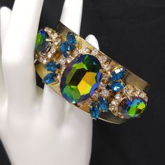 *Description: This is a gorgeous watermelon rhinestone crystal bracelet on a golden brass cuff which glitters and sparkles in the light. The vintage rhinestones are secured on a golden brass cuff and the reflective cuff adds additional sparkle to the bracelet. There is one large watermelon rhinestone in the center, surrounded by clear rhinestones and sapphire blue marquise cut rhinestones. On each side of the center stone are two more watermelon rhinestones, a little smaller in size, one on each Metal Crystal Bracelet With Stones For Party, Party Crystal Bracelet With Metal Stones, Party Crystal Bracelet With Stones, Crystal Bangle Cuff Bracelet For Party, Gold Jeweled Bangle For Party, Glamorous Jeweled Bracelets For Party, Gold Party Bangle With Jewels, Party Gold Bangle With Jewels, Gold Crystal Cuff Bracelet Bangle