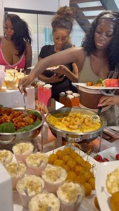 a group of women standing around a table filled with different types of food and drinks