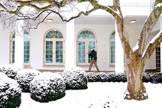 a man walking in front of a white building with snow on the ground and trees