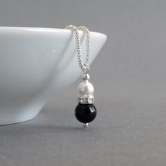 Simple and elegant in design, this black onyx and white pearl necklace would be ideal for bridesmaids in a monochrome themed wedding. A lone, white glass pearl sits in a crystallised band above a jet black onyx bead. This glass pearl and crystal teardrop hangs from a Sterling silver corb chain.  The 18 inch corb chain is a more ornate alternative to the standard snake chain. The way the chain is cut and assembled means it really glimmers in the light. The pearl drop pendant measures 2.3cm high a Elegant Black Pendant Pearl Necklace, Elegant Black Pearl Necklace For Weddings, Black Pearl Drop Necklace For Gift, Elegant Black Pearl Necklace For Gift, Elegant Black Drop Necklace Gift, Formal Black Necklace With Pearl Pendant, Formal Black Pearl Pendant Necklace, Black Pearl Necklace For Wedding, Elegant Black Bridal Necklace For Formal Occasions