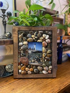 a wooden frame with rocks and stones in it on a table next to a potted plant