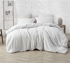 a bed with white linens and pillows in a room next to a brick wall