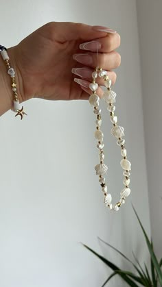 a woman's hand holding a beaded bracelet with seashells and starfish charms