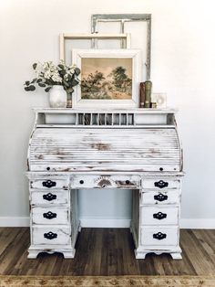 an old white desk with drawers and a painting on the wall next to it in a room