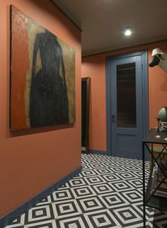 an orange room with black and white flooring, paintings on the walls and a blue door