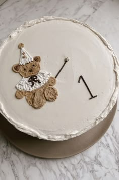 a white cake decorated with a teddy bear on it's side and an arrow in the middle