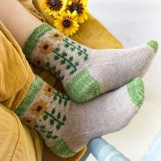 the legs of a person wearing socks with green and yellow designs on them, next to a sunflower