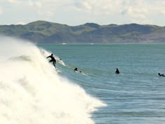 several surfers are riding the waves on their surfboards in the ocean with mountains in the background