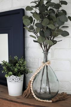 a vase filled with green plants on top of a wooden table next to a potted plant