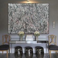 an abstract painting hangs on the wall above two stools in front of a glass table