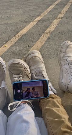 two people sitting on the ground with their feet crossed and one person holding a cell phone