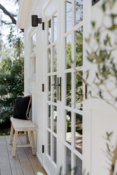 a wooden bench sitting on the side of a white house next to a door and windows