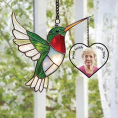 a stained glass hummingbird hanging from a chain with a heart on it's side