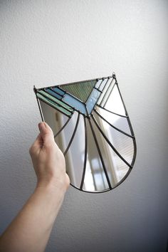 a hand is holding a stained glass fan in front of a mirror on the wall