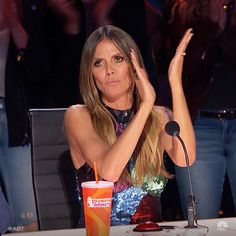 a woman sitting at a table in front of a microphone and holding her hand up