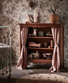 an old fashioned bookcase with pink curtains in a room filled with furniture and wallpaper