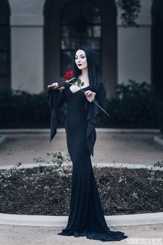 a woman dressed in black holding a rose and posing for a photo on instagram