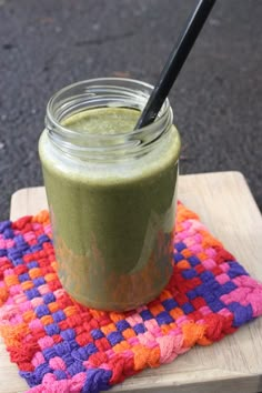 a green smoothie in a mason jar with a black straw on a colorful placemat