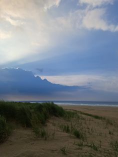 the beach is covered in grass and sand as the sun shines through the clouds