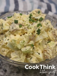 a glass bowl filled with potato salad on top of a granite counter next to a blue and white towel