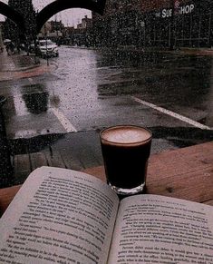 an open book sitting on top of a wooden table next to a cup of coffee