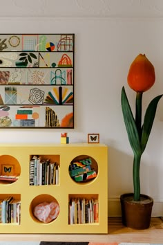 a yellow book shelf with books on it and a flower in the corner next to it