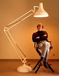 a person sitting in a chair with a lamp on the floor next to him and his legs crossed