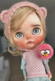 a close up of a doll with a bird on it's shoulder and wearing a pink knitted hat