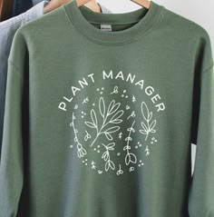 Gardeners will love this cute Plant Manager Shirt! Perfect for gardening or spending time at the farmers market! * 50% cotton, 50% polyester * Pre-shrunk * Classic fit * 1x1 athletic rib knit collar with spandex * Air-jet spun yarn with a soft feel and reduced pilling * Double-needle stitched collar, shoulders, armholes, cuffs, and hem * Wash inside out in cool water See more trendy styles here: www.etsy.com/shop/QueenBeaDesignCo Plant Lover Shirt Ideas, Spring Green Tops With Plant Details, Plant Tshirt Design, Green Tops With Plant Print For Gardening, Green Plant Print Tops For Gardening, Green Cotton Cottagecore Tops, Cottagecore Green Cotton Top, Gardening Tshirt, Gardening Shirt