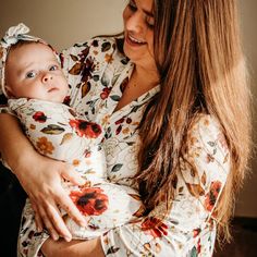 a woman holding a baby in her arms and smiling at the camera while wearing a floral shirt