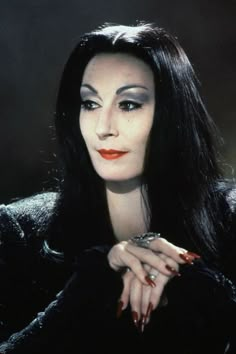 a woman with long black hair and red nails posing for a photo in front of a dark background