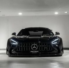 the front end of a black mercedes sports car in a white room with lights on