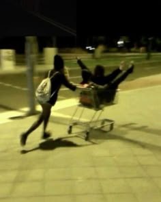 two people pushing a shopping cart down the street at night, with their arms in the air