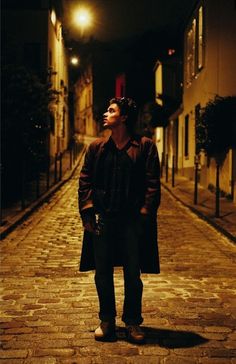 a man standing on a cobblestone street at night with his head in the air