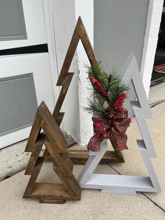 three wooden christmas trees sitting next to each other on the ground near a house door