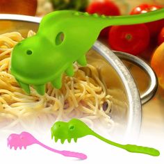 a green plastic toy is in a bowl of noodles with tomatoes and peppers on the side