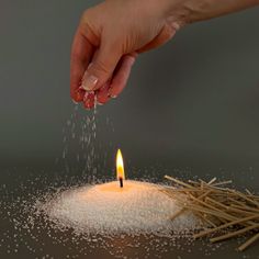 a person sprinkling sugar over a lit candle on top of a pile of straw