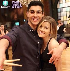 a man and woman posing for a photo in front of drumsticks on the dance floor