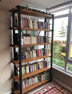 a bookshelf filled with lots of books in front of a window next to a rug