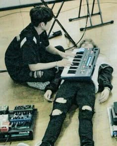 a young man sitting on the floor playing an electronic keyboard while another person sits next to him