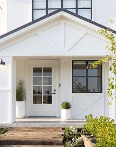 a white house with two plants in pots on the front door and steps leading up to it