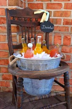 a bucket filled with drinks sitting on top of a wooden chair next to a brick wall