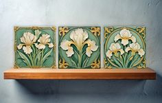 three tiles with flowers on them sitting on top of a wooden shelf next to a wall