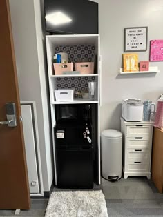 a room with a black refrigerator and some white drawers on the wall next to it