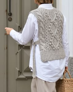 a woman wearing a knitted vest and holding a basket in front of a door