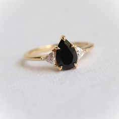 This Alexis Ring is designed for the modern woman, with a classic black onyx stone set in a chic and timeless 3-stone style setting, featuring intricate triangular stone accents. Let this statement piece bring cool sophistication to any look. ---------------------- ✦ CENTER STONE： Natural Black Onyx ✧ Shape： Pear ✧ Size：9 x 6 mm ✧ Carat Weight：1.5 ct Approx. ✦ SIDE STONE: Lab-Created Moissanite DEF ✧ Shape： Triangle ✧ Size: 3.5 mm  ✦ SETTING: ✧ Metal: Choice of 14k/18k yellow/white/rose or Plati Timeless Black Jewelry With Center Stone, Timeless Black Wedding Rings, 14k Gold Black Ring With Center Stone, Black Teardrop Wedding Rings, Black 14k Gold Ring With Center Stone, Classic Black Pear-shaped Jewelry, Elegant Black Pear-shaped Jewelry, Elegant Onyx Rings With Diamond Accents, Black Pear-shaped Ring For Anniversary