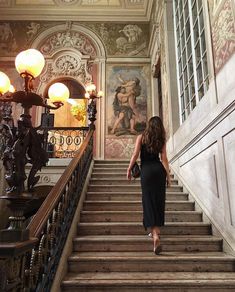 a woman is walking down the stairs in an old building with paintings on the walls