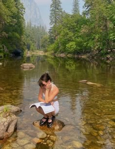 a woman sitting on top of a rock next to a river